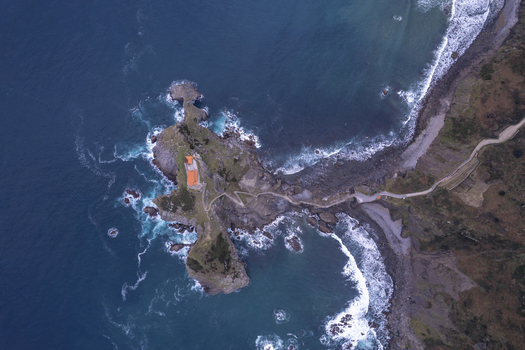 Aerial view of San Juan de Gaztelugatxe a historic hermitage on a rocky islet connected by a winding stone bridge to the rugged coastline of Gaztelugatxeko Doniene Euskadi Spain.