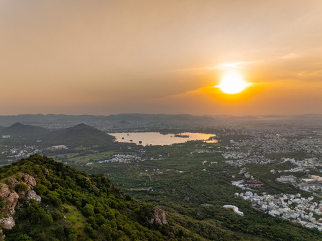 Aerial view of the city of Udaipur surrounded by lush green hills and a shimmering lake at sunset in Udaipur Rajasthan India.