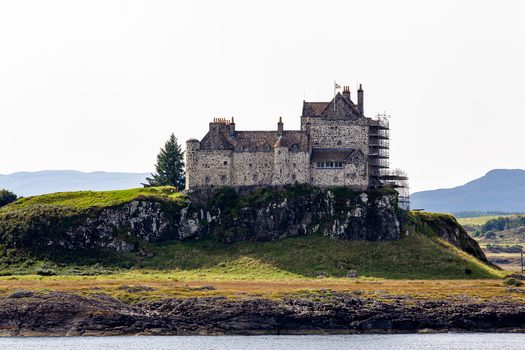 View of Duart Castle a historic stone fortress situated on a rocky cliff overlooking the water with rolling hills in the background in Isle of Mull Scotland United Kingdom.