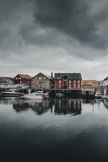 View of colorful traditional wooden houses and boats reflected in the calm harbor water of Henningsvaer Nordland Norway. View of colorful traditional wooden houses and boats reflected in the calm harbor water of Henningsvaer Nordland Norway.