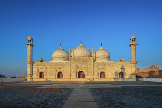 View of the historic Abbasi Mosque with its white marble domes and minarets under a clear blue sky in the courtyard of Derawar Punjab Pakistan.