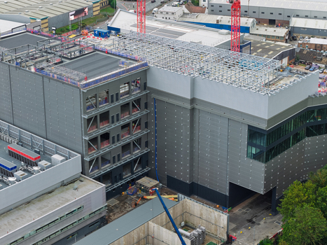 Aerial view of a large data center under construction featuring a steel framework industrial cladding and cranes on site in the United Kingdom.