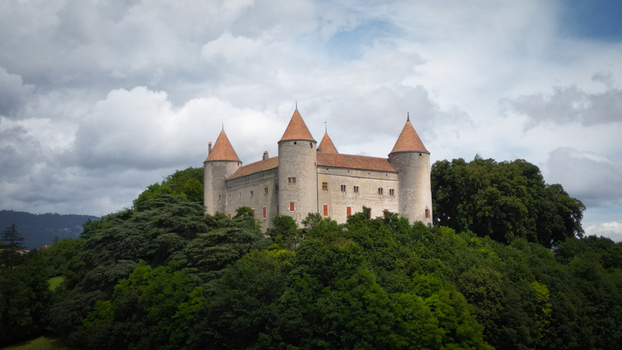 Aerial view of the ancient castle a fortress of stone and history rises majestically amidst a sea of verdant trees under a sky brushed with clouds Champvent Vaud Switzerland. Aerial view of the ancient castle a fortress of stone and history rises majestically amidst a sea of verdant trees under a sky brushed with clouds Champvent Vaud Switzerland.