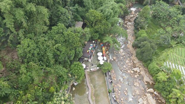 Aerial view of Kopi Tubing Cafe and Resto nestled in lush greenery alongside a rocky river with white umbrellas and visitors in Kecamatan Pamijahan Jawa Barat Indonesia. Aerial view of Kopi Tubing Cafe and Resto nestled in lush greenery alongside a rocky river with white umbrellas and visitors in Kecamatan Pamijahan Jawa Barat Indonesia.