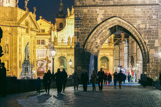 Prague Czechia 03 November 2021 View of the historic Charles Bridge at night with pedestrians walking under the stone archway illuminated by warm street lamps. Prague Czechia 03 November 2021 View of the historic Charles Bridge at night with pedestrians walking under the stone archway illuminated by warm street lamps.
