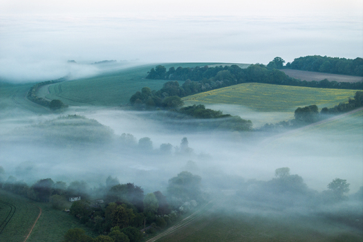 Aerial view of rolling green hills and lush fields shrouded in thick morning mist and fog Nuffield Oxfordshire United Kingdom. Aerial view of rolling green hills and lush fields shrouded in thick morning mist and fog Nuffield Oxfordshire United Kingdom.