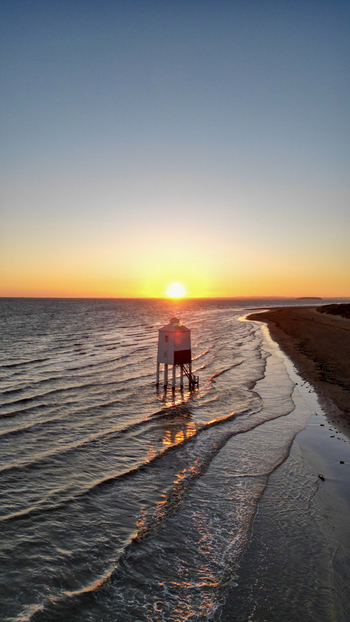 Aerial view of the historic Burnham on Sea Low Lighthouse standing in the sea at sunset with gentle waves washing onto the sandy beach in Burnham on Sea England United Kingdom. Aerial view of the historic Burnham on Sea Low Lighthouse standing in the sea at sunset with gentle waves washing onto the sandy beach in Burnham on Sea England United Kingdom.