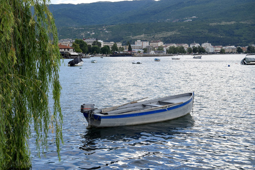 View of a small wooden boat floating on the calm waters of Lake Ohrid with the historic town and mountains in the background Ohrid Municipality of Ohrid North Macedonia. View of a small wooden boat floating on the calm waters of Lake Ohrid with the historic town and mountains in the background Ohrid Municipality of Ohrid North Macedonia.