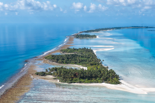 Aerial view of lush tropical islands with green palm trees and turquoise coral reefs surrounded by the deep blue ocean under a clear sky near Vaanee Dhaalu Atoll Maldives. Aerial view of lush tropical islands with green palm trees and turquoise coral reefs surrounded by the deep blue ocean under a clear sky near Vaanee Dhaalu Atoll Maldives.