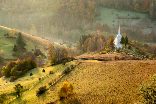 View of a rural church nestled on a hillside surrounded by autumn trees and rolling meadows under warm golden hour light in Alba Iulia Alba County Romania. View of a rural church nestled on a hillside surrounded by autumn trees and rolling meadows under warm golden hour light in Alba Iulia Alba County Romania.