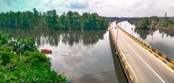 Aerial view of a bridge spanning a wide river surrounded by lush tropical vegetation and a small boat with people Buguma Rivers Nigeria.