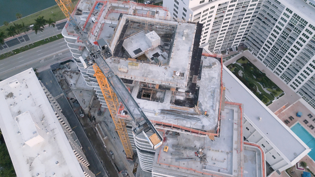 Aerial view of a high rise building under construction featuring a large yellow tower crane and concrete framework in the urban landscape of Miami Beach Florida United States. Aerial view of a high rise building under construction featuring a large yellow tower crane and concrete framework in the urban landscape of Miami Beach Florida United States.