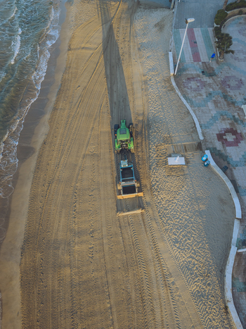 Aerial view of a tractor raking the sand on the beach with visible tire tracks along the shoreline in Calp Valencian Community Spain. Aerial view of a tractor raking the sand on the beach with visible tire tracks along the shoreline in Calp Valencian Community Spain.