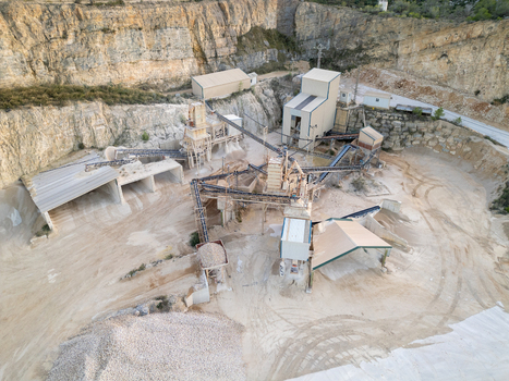 Aerial view of an industrial stone quarry with processing machinery conveyor belts and piles of gravel set against a rocky cliff face in Teulada Valencian Community Spain.