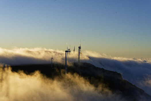 Aerial view of wind turbines at Bica da Cana peak and viewpoint rising above a thick layer of clouds during golden hour in Funchal Madeira Portugal.