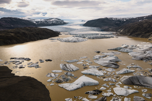 Aerial view of Vatnajokull glacier with icebergs floating in a glacial lake surrounded by dark volcanic mountains in Iceland.