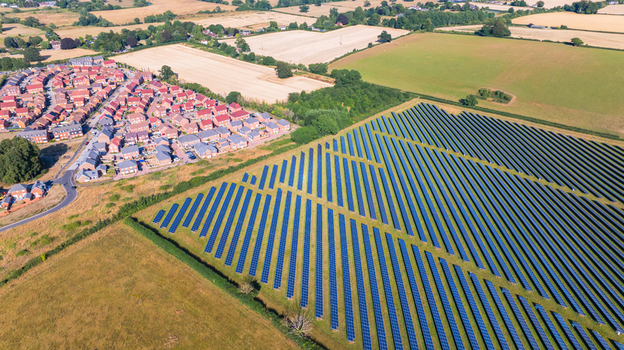 Aerial view of a large solar farm with rows of photovoltaic panels adjacent to a residential neighborhood with houses and green fields in Dorset England United Kingdom. Aerial view of a large solar farm with rows of photovoltaic panels adjacent to a residential neighborhood with houses and green fields in Dorset England United Kingdom.
