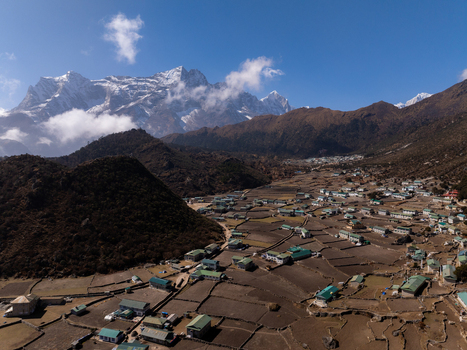 Aerial view of a mountain village with terraced fields and houses with green roofs nestled in the Himalayas in Nepal.