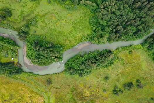 Aerial view of a winding river flowing through lush green meadows and dense coniferous forests in the wilderness of Juneau Alaska United States. Aerial view of a winding river flowing through lush green meadows and dense coniferous forests in the wilderness of Juneau Alaska United States.