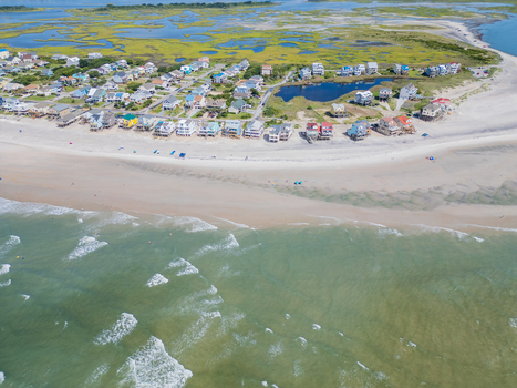 Aerial view of coastal houses lining the sandy beach with a marshland area and the Atlantic Ocean in North Topsail Beach North Carolina United States.