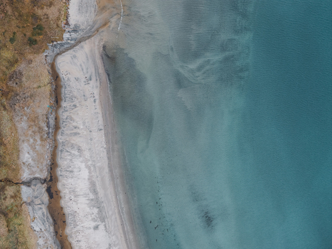 Aerial view of the coastline of Senja showcasing the contrast between the sandy beach clear turquoise waters and the rugged terrain of the island in Senja Troms Norway.