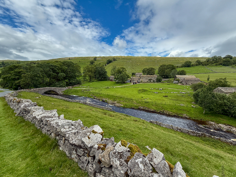 View of a traditional stone bridge and dry stone walls in the lush green countryside with rolling hills and stone farmhouses Hawes England United Kingdom. View of a traditional stone bridge and dry stone walls in the lush green countryside with rolling hills and stone farmhouses Hawes England United Kingdom.