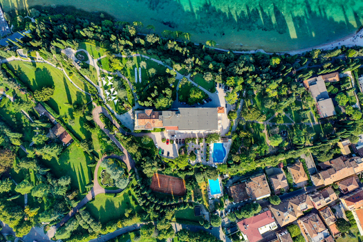 Aerial view of Villa Cortine Palace Hotel featuring swimming pools and tennis courts surrounded by lush gardens on the shore of Lake Garda in Sirmione Lombardia Italy. Aerial view of Villa Cortine Palace Hotel featuring swimming pools and tennis courts surrounded by lush gardens on the shore of Lake Garda in Sirmione Lombardia Italy.