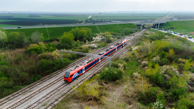 Aerial view of a vibrant red and blue train slicing through the landscape near a bridge contrasting with the green fields Sremska Mitrovica Vojvodina Serbia. Aerial view of a vibrant red and blue train slicing through the landscape near a bridge contrasting with the green fields Sremska Mitrovica Vojvodina Serbia.
