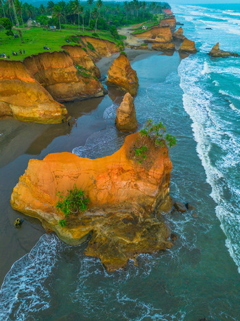Aerial view of dramatic orange coastal cliffs and rock formations rising from the turquoise ocean waves along the sandy beach in Bali Bali Indonesia. Aerial view of dramatic orange coastal cliffs and rock formations rising from the turquoise ocean waves along the sandy beach in Bali Bali Indonesia.