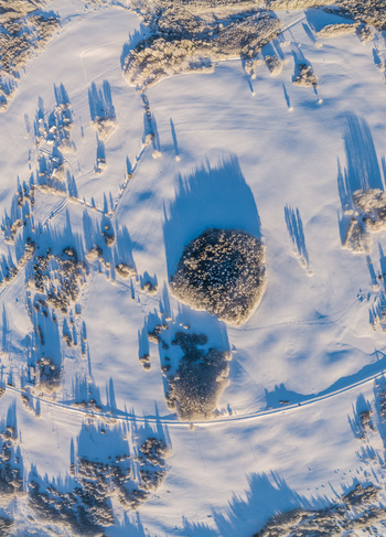 Aerial view of a snow covered landscape in Latvia with frost covered trees long shadows cast by the low winter sun and a winding road cutting through the white fields Latvia. Aerial view of a snow covered landscape in Latvia with frost covered trees long shadows cast by the low winter sun and a winding road cutting through the white fields Latvia.