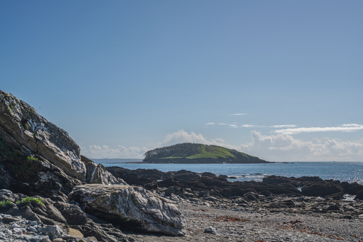 View of the South West Coastal Path overlooking the rocky coastline and Portnadler Bay under a clear blue sky in Looe Cornwall United Kingdom. View of the South West Coastal Path overlooking the rocky coastline and Portnadler Bay under a clear blue sky in Looe Cornwall United Kingdom.
