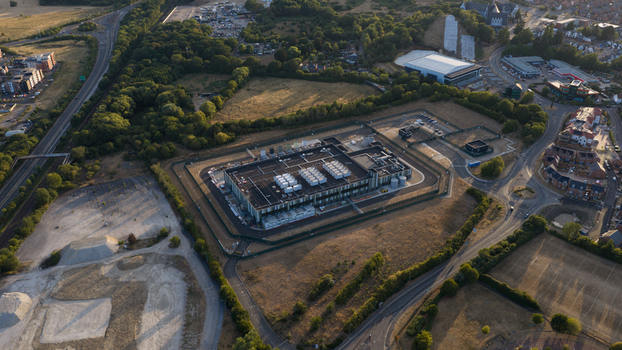 Aerial view of a large data center facility surrounded by security fencing access roads and surrounding green landscape in Bracknell England United Kingdom.