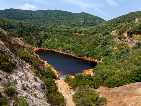 Aerial view of Laghetto delle Conche also known as Lago di Sangue featuring its distinctive dark red water surrounded by lush green hills and rocky terrain in Rio Marina Toscana Italy.