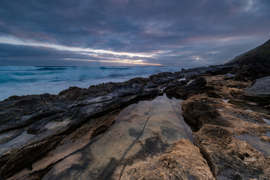 View of the rocky coastline with tidal pools and crashing waves under a dramatic cloudy sky at dusk in Sandpatch Western Australia Australia. View of the rocky coastline with tidal pools and crashing waves under a dramatic cloudy sky at dusk in Sandpatch Western Australia Australia.