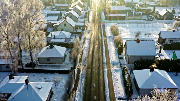Aerial view of a quiet residential street lined with snow covered houses and frost covered trees during a bright winter day in Latvija. Aerial view of a quiet residential street lined with snow covered houses and frost covered trees during a bright winter day in Latvija.
