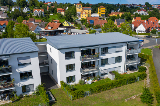 Aerial view of modern white apartment buildings with grey roofs and balconies overlooking a residential neighborhood on a sunny day in Erlangen Bavaria Germany.