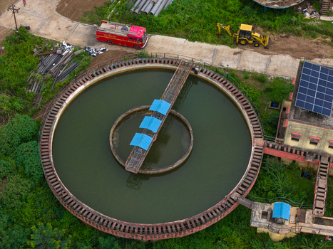 Aerial view of a circular water treatment tank with a central metal walkway and blue roofs featuring a fire truck and construction equipment nearby in Karad Maharashtra India.