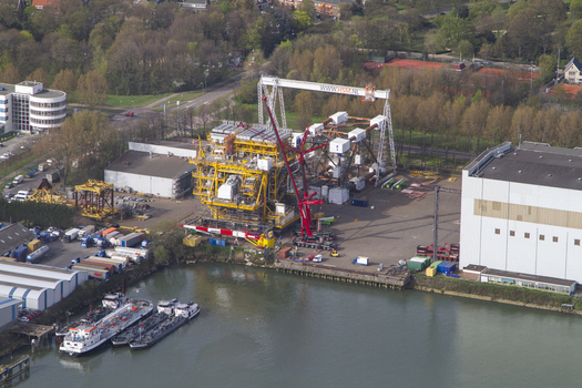 Aerial view of an industrial facility at Rotterdam Harbour with a large yellow offshore platform a red crane and cargo barges in the canal in Rotterdam South Holland Netherlands. Aerial view of an industrial facility at Rotterdam Harbour with a large yellow offshore platform a red crane and cargo barges in the canal in Rotterdam South Holland Netherlands.