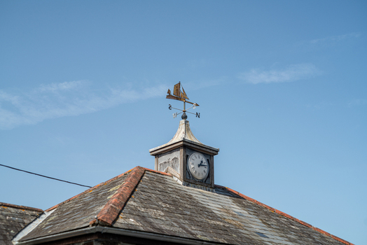 View of a clock tower with a sailboat weather vane atop a slate roof in the coastal village of Polperro Cornwall United Kingdom. View of a clock tower with a sailboat weather vane atop a slate roof in the coastal village of Polperro Cornwall United Kingdom.