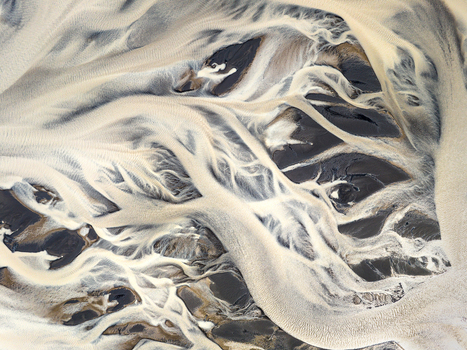 Aerial view of a braided river system with intricate glacial sediment patterns flowing through black volcanic sand in Iceland. Aerial view of a braided river system with intricate glacial sediment patterns flowing through black volcanic sand in Iceland.