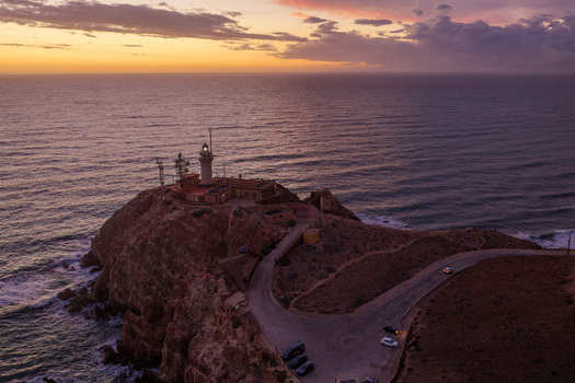 Aerial view of Lighthouse de Cabo de Gata perched on a rocky cliff overlooking the sea during a vibrant sunset with a winding road and parked cars in San Jose Andalucia Spain. Aerial view of Lighthouse de Cabo de Gata perched on a rocky cliff overlooking the sea during a vibrant sunset with a winding road and parked cars in San Jose Andalucia Spain.