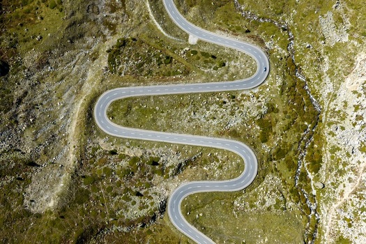 Aerial view of the winding road of Julier Pass with sharp curves rocky alpine terrain and green mountain slopes in Surses Grisons Switzerland.