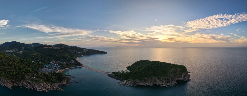 Aerial view of Ko Pha Ngan island with a sandbar connecting to the lush coastline surrounded by calm sea under a golden sunset sky Ko Pha ngan District Surat Thani Thailand.