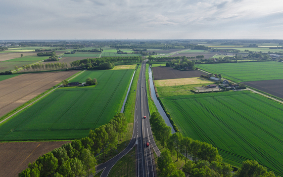 Aerial view of a straight highway with cars cutting through vibrant green agricultural fields and meadows. Aerial view of a straight highway with cars cutting through vibrant green agricultural fields and meadows.