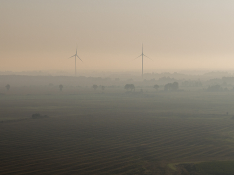 Aerial view of two wind turbines standing in a misty landscape over agricultural fields during a hazy sunrise Taujenai Vilnius County Lithuania.