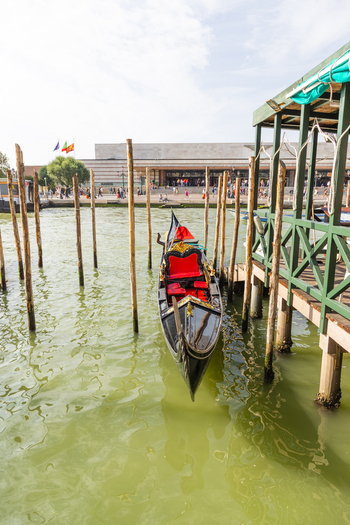 Venice Italy 21 September 2026 View of a traditional black gondola with red velvet seats moored at a wooden pier in the Grand Canal with the Santa Lucia station in the background. Venice Italy 21 September 2026 View of a traditional black gondola with red velvet seats moored at a wooden pier in the Grand Canal with the Santa Lucia station in the background.