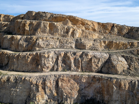 Aerial view of a large open pit stone quarry with terraced rock walls and dirt access roads under a clear blue sky in Teulada Valencian Community Spain.