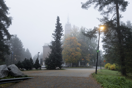 View of a building with a clock tower surrounded by pine trees and autumn foliage in a foggy park setting in Jyvaskyla Central Finland Finland.