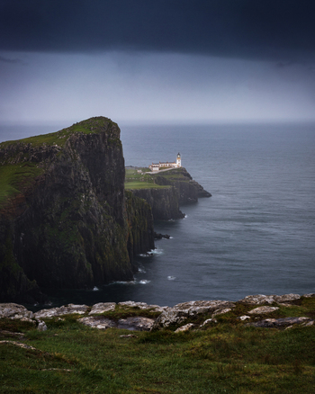 View of Neist Point Lighthouse perched on dramatic cliffs under a dark stormy sky overlooking the Atlantic Ocean in Isle of Skye Scotland United Kingdom.