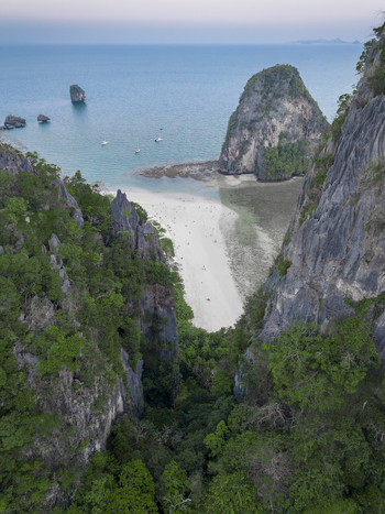 Aerial view of the craggy limestone cliffs framing the serene white sands and turquoise waters of Railay Beach Krabi Thailand.